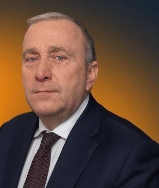 Grzegorz Schetyna podczas spotkania politycznego, aktywnie gestykulujący, w tle zamazane postacie.