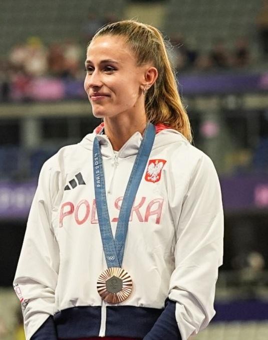 Natalia Bukowiecka uśmiechająca się, w spokojnej, codziennej scenerii, z delikatnie rozmyty tłem.