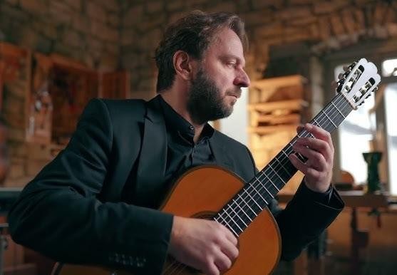 Marcin Dylla grający na gitarze klasycznej na scenie, w dynamicznym ujęciu, w świetle reflektorów.