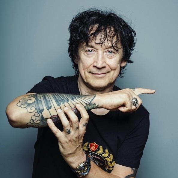 Jan Borysewicz w młodości, grający na gitarze elektrycznej na scenie, pełen energii i charyzmy, w typowym stroju rockowym z lat 80.
