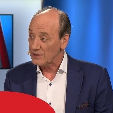 Ręka Dariusza Szpakowskiego trzymająca mikrofon, z rozmytym tłem stadionu piłkarskiego, symbolizująca jego obecność na wydarzeniach sportowych.