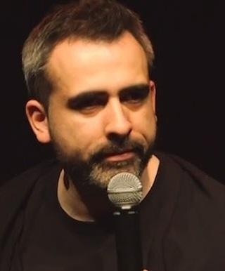 Abelard Giza na scenie, w dynamicznej pozie, symbolizującej jego karierę komika i stand-upera.