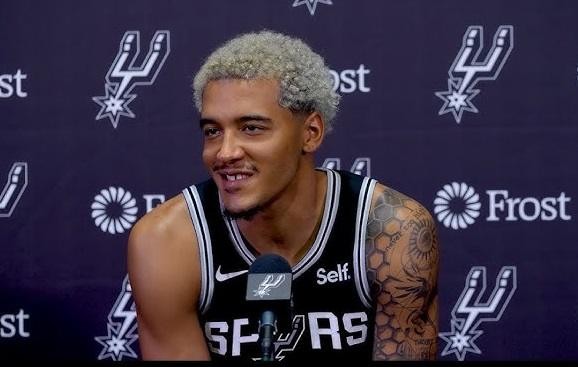 Jeremy Sochan w dynamicznym ujęciu akcji na boisku koszykarskim, w stroju San Antonio Spurs, prezentujący swój atletyzm i unikalny styl gry.