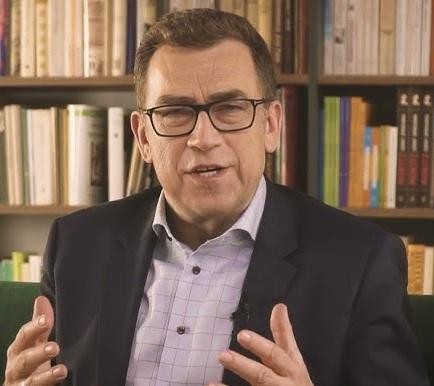 Maciej Orłoś podczas szkolenia z wystąpień publicznych, gestykulujący z mikrofonem, z widownią w tle.