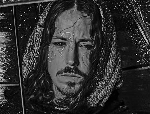 Michał Szpak w zbliżeniu, z długimi włosami i charakterystycznym makijażem, z intensywnym spojrzeniem.