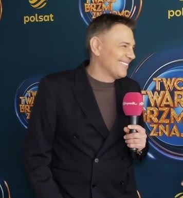 Krzysztof Ibisz w dynamicznej pozie na scenie, prezentujący swoją charyzmę i energię.